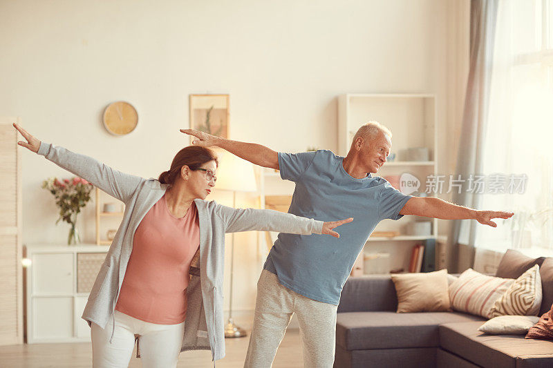 Content senior couples in activewear standing in living room and outstretch arms while together at home .内容老年夫妇穿着运动服站在客厅里，在家里一起伸展手臂训练